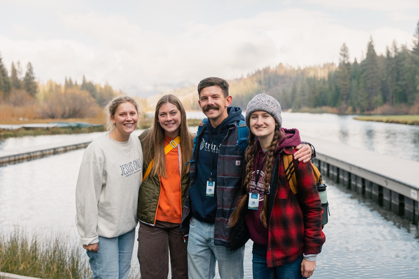 Four summer staff arm in arm on the dock at Hume Lake in autumn.