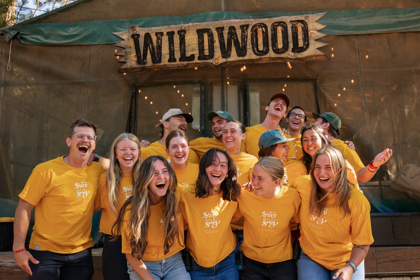Wildwood summer staff in yellow shirts cheering under the Wildwood sign.
