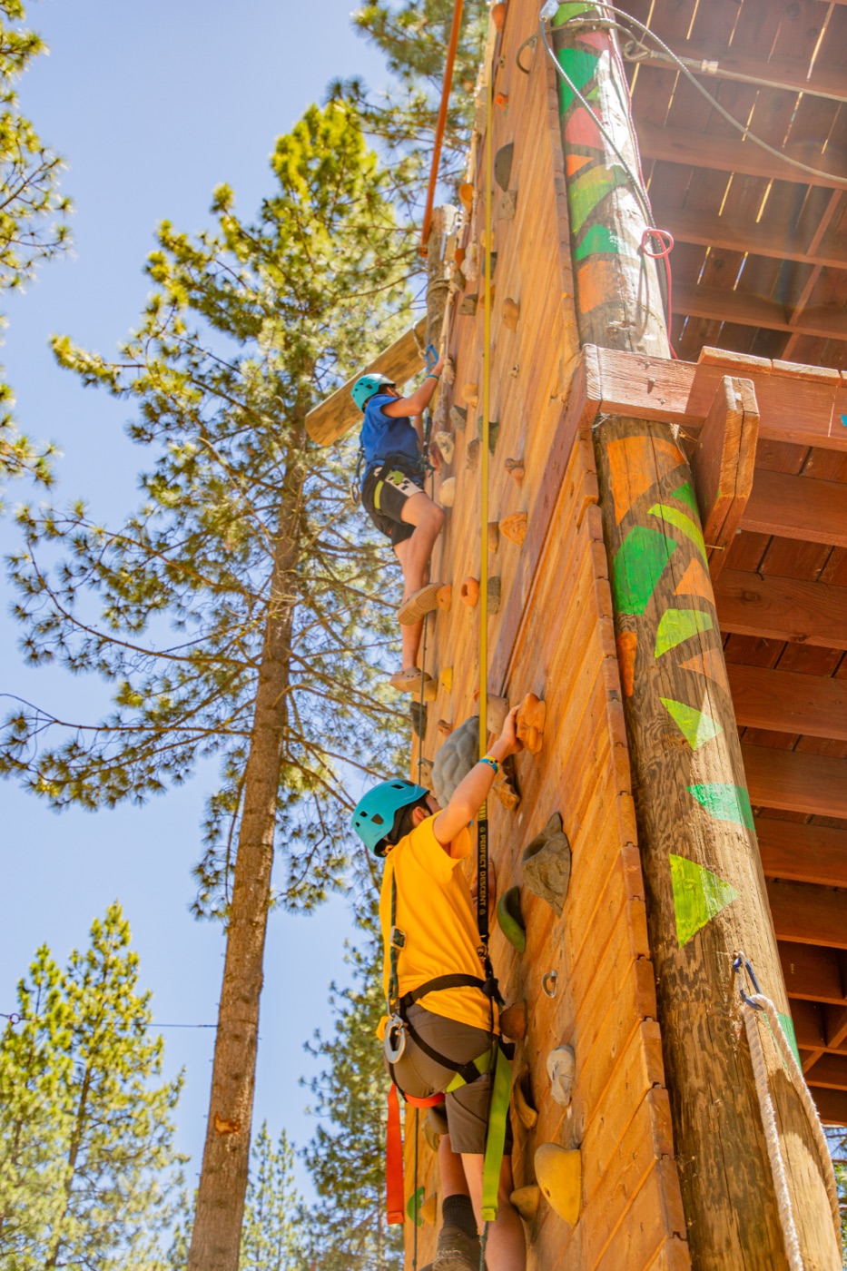 A camper climbing the high ropes tower among the pines.