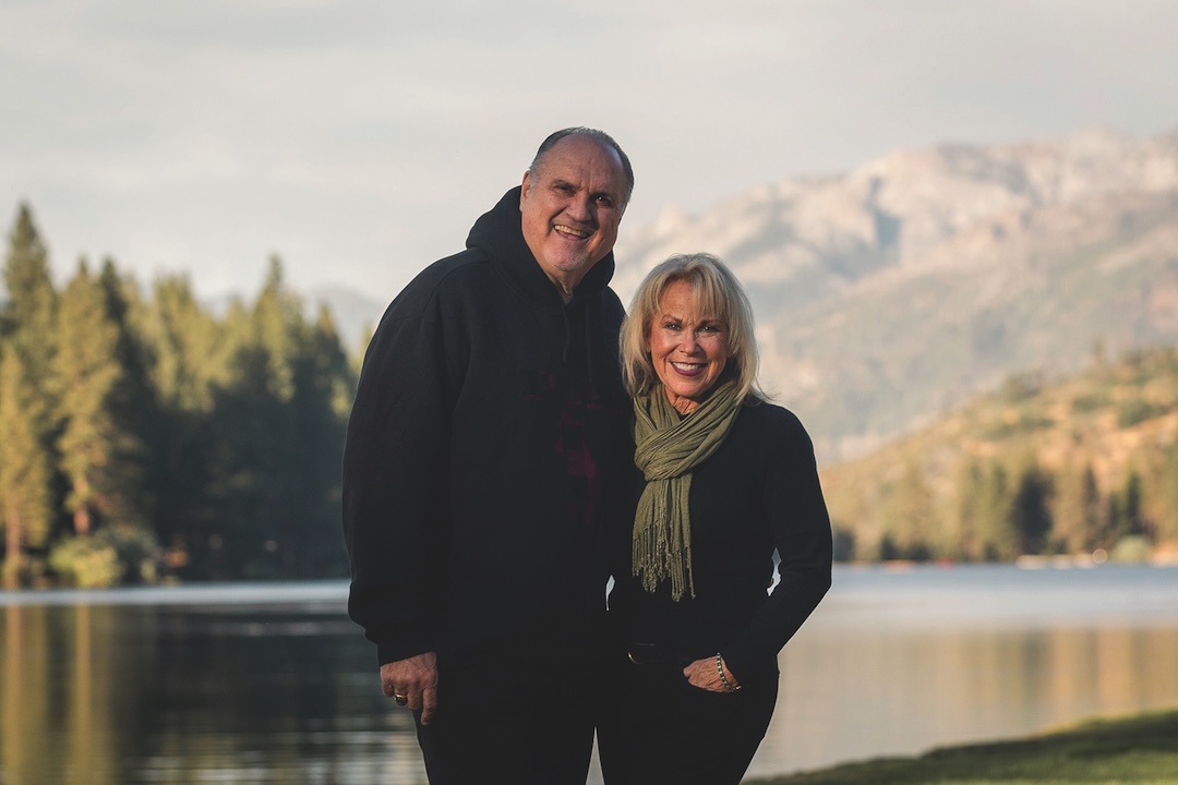 John and Lyn Boal smiling by the lake at Hume, pines and the Sierra behind them.